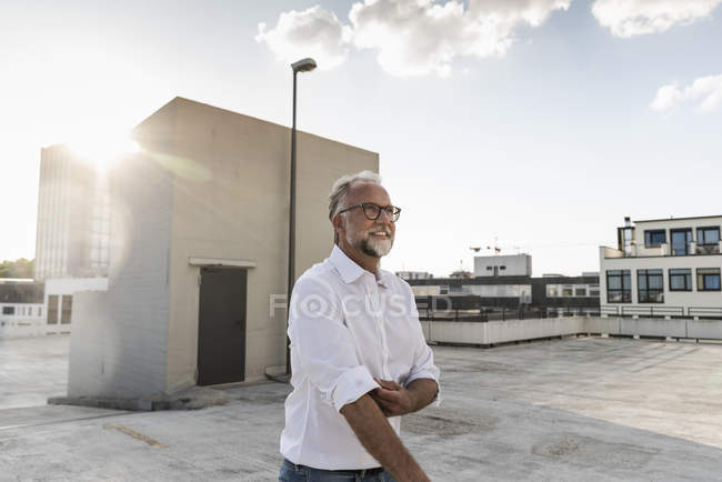 Зрілий чоловік стоїть на даху багатоповерхової будівлі, згорнутий рукавами — стокове фото