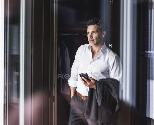 Бізнесмен з мобільним телефоном, стоячи в гардеробі вдома — стокове фото