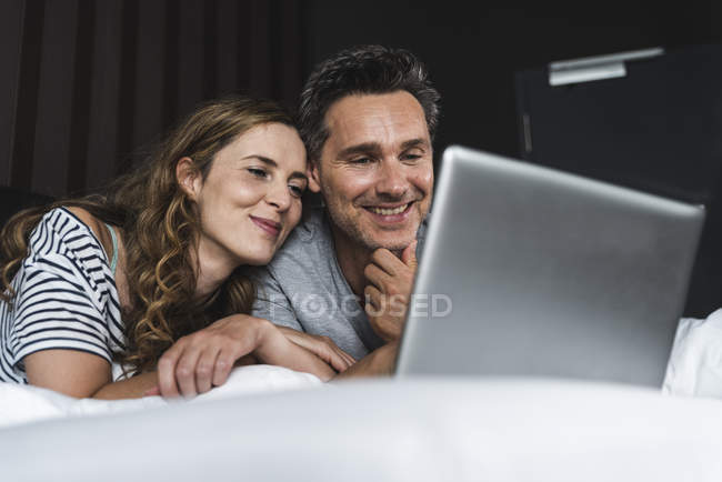 Щаслива пара лежав на ліжку в будинку, дивлячись на ноутбук — стокове фото