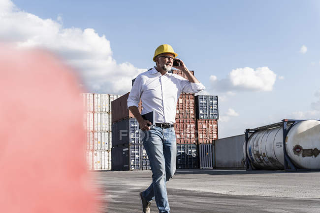 Бизнесмен в грузовой гавани, защитный шлем, используя смартфон и цифровой планшет — стоковое фото