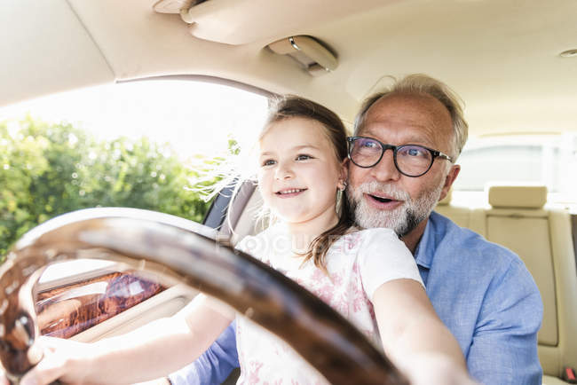 Ragazzina seduta sulle ginocchia del nonno, fingendo di guidare l'auto — Foto stock