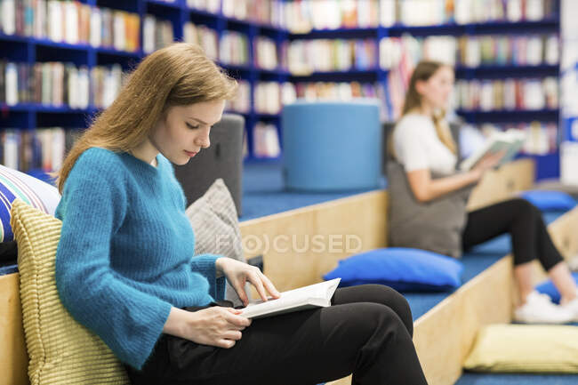 Teenage girls sitting in a public library reading book — Stock Photo