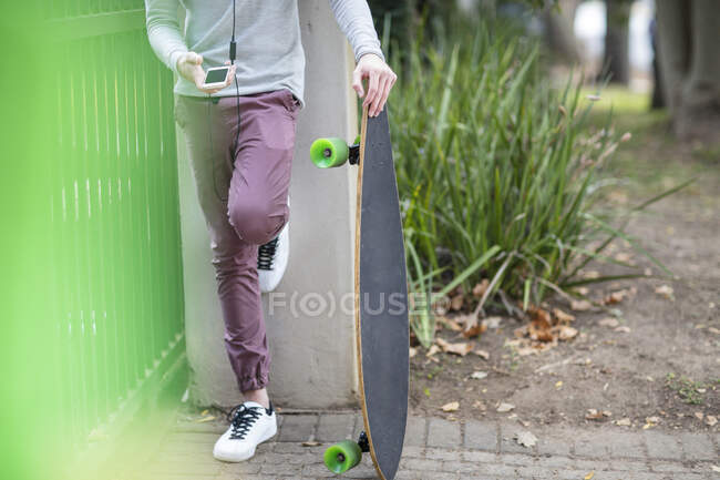 Primo piano del ragazzo che tiene lo skateboard e utilizza il telefono cellulare — Foto stock
