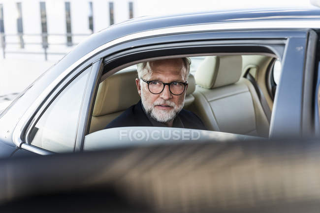 Mature businessman sitting on backseat in car, looking out of window — Stock Photo