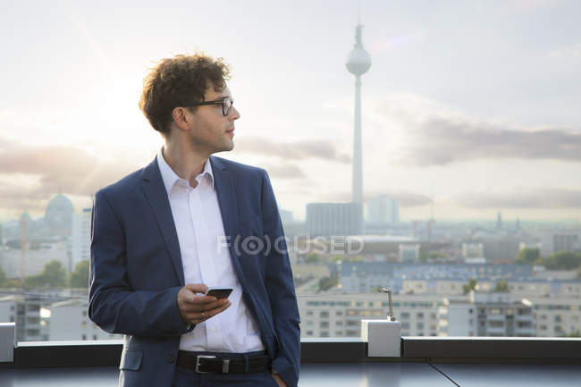 Deutschland, berlin, unternehmer mit smartphone am abend auf dachterrasse — Stockfoto
