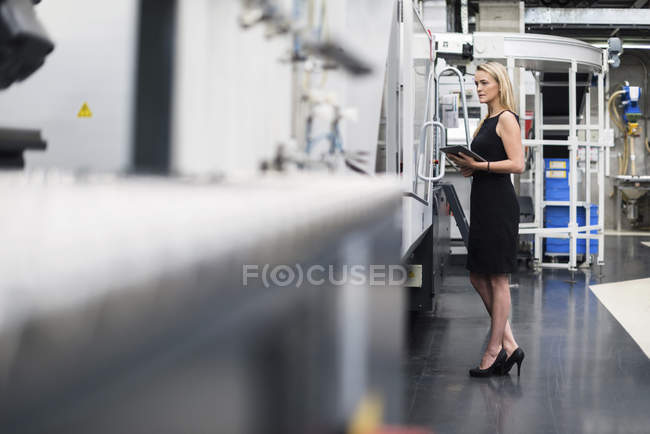 Женщина с помощью планшета на станке в цехе завода — стоковое фото