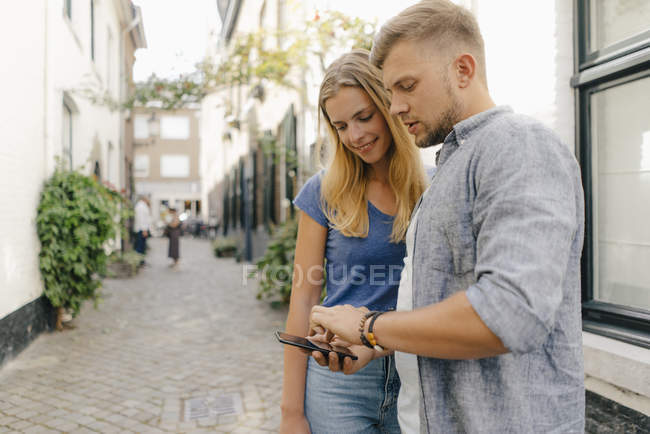 Netherlands, Maastricht, young couple looking at cell phone the city — Stock Photo
