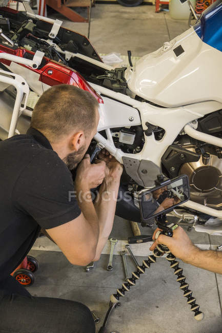 Механіка роботи на мотоциклі в майстерні, знятому його партнером. — стокове фото