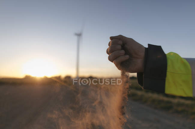 Close-up of man scattering soil at a wind turbine at sunset — Stock Photo