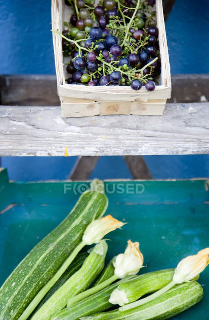 Ladder, basket with blue grapes, box with zucchini and blossoms — Stock Photo