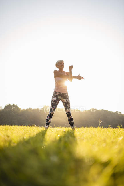 Senior woman stretching on rural meadow at sunset — Stock Photo