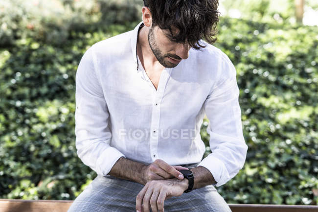 Young man sitting outdoors and looking at smartwatch — Stock Photo