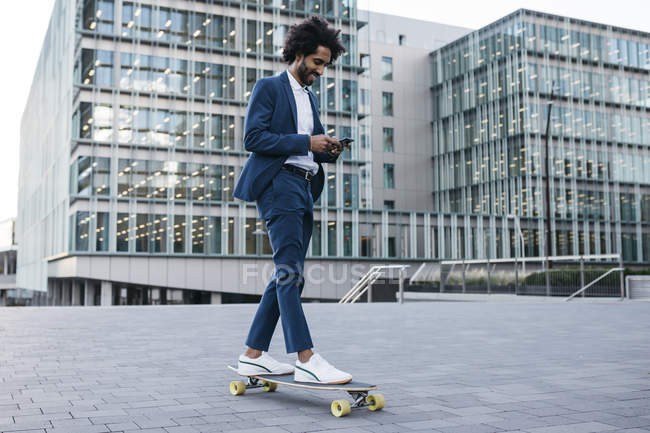 Іспанія, Барселона, молодий бізнесмен їзда скейтборд і використання мобільного телефону в місті — стокове фото
