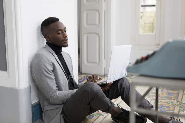 Retrato de jovem empresário sentado no chão no escritório, trabalhando em laptop — Fotografia de Stock