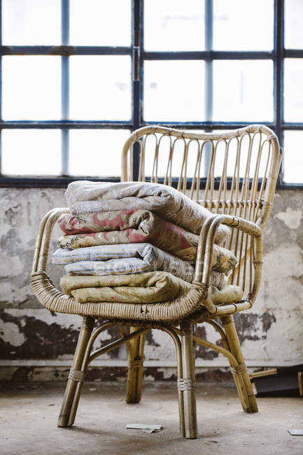 Stack of various blankets on basket-chair in a loft — Stock Photo