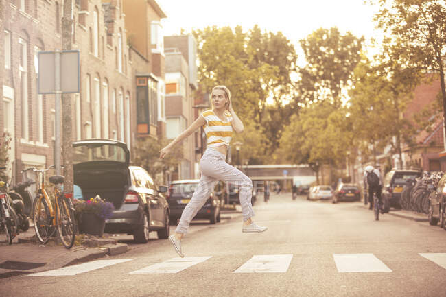 Junge Frau springt auf Zebrastreifen in die Luft — Stockfoto