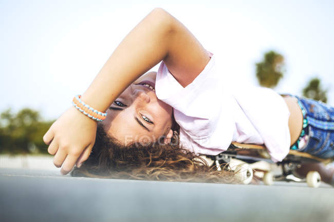 Ragazza sdraiata su skateboard, guardando la fotocamera — Foto stock