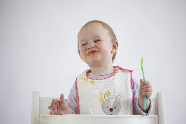 Portrait of smiling baby girl on high chair eating mush — Stock Photo