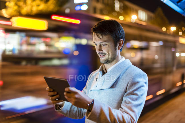 Портрет улыбающегося бизнесмена, смотрящего на цифровой планшет на улице ночью — стоковое фото
