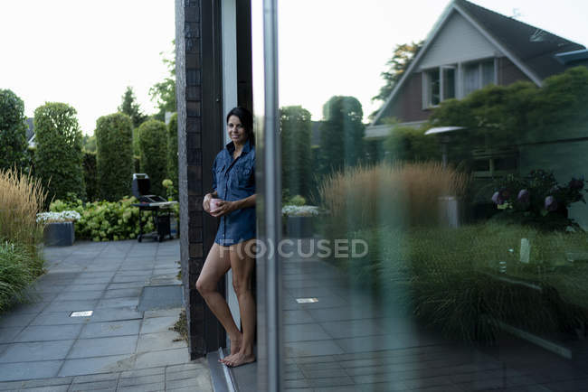 Femme debout sur la terrasse d'une maison moderne et tenant une tasse — Photo de stock