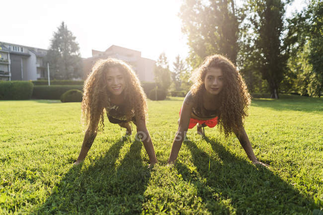 Hermanas gemelas haciendo flexiones en un prado - foto de stock