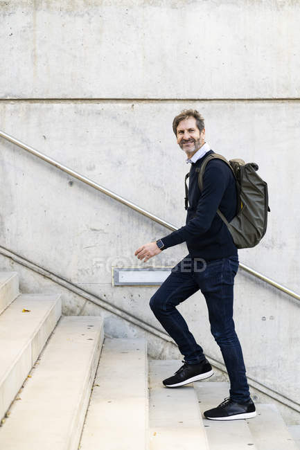 Smiling mature man with a backpack walking up stairs in the city — Stock Photo