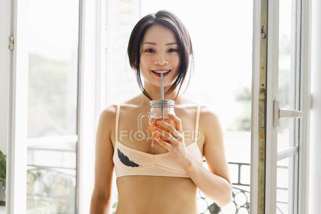 Porträt einer attraktiven jungen Frau mit BH und einem Drink am Fenster — Stockfoto