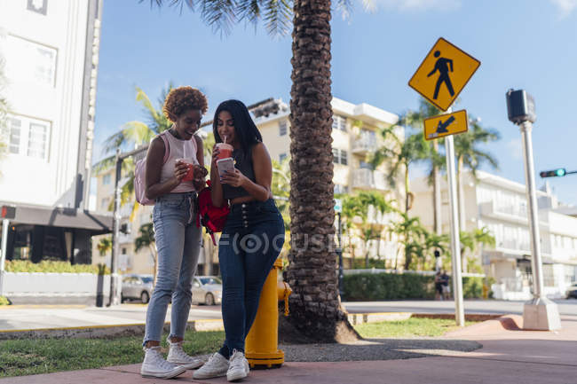 États-Unis, Floride, Miami Beach, deux amies heureuses avec téléphone portable et boisson gazeuse dans la ville — Photo de stock