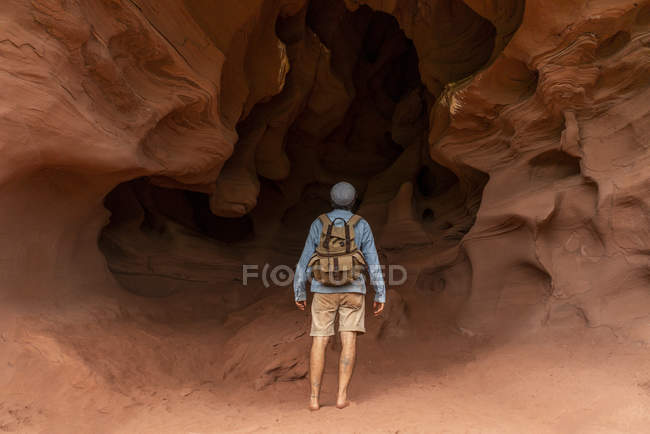 Young man with backpack, looking at cave, rear view — Stock Photo