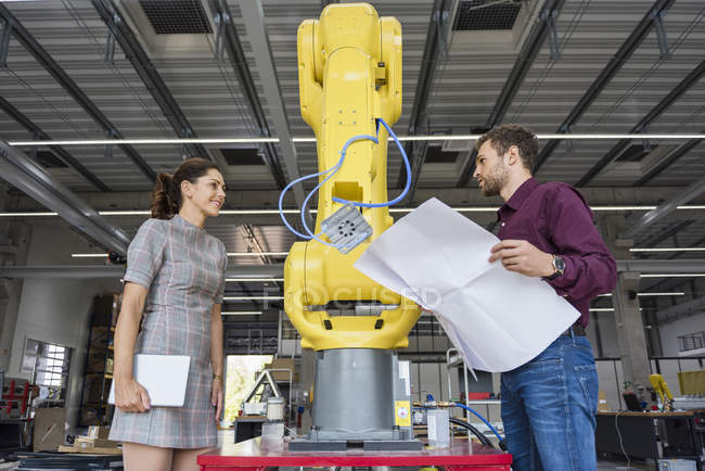 Empresario y mujer teniendo una reunión frente a robots industriales en una empresa de alta tecnología - foto de stock