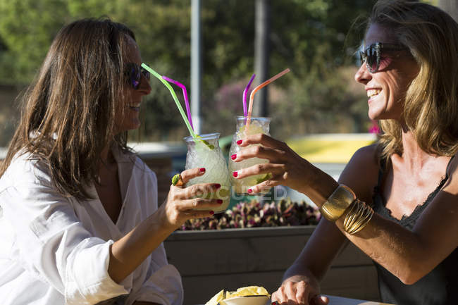 Felices amigas sentadas al aire libre con gafas de cóctel - foto de stock