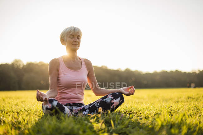 Donna anziana in posizione di loto sul prato rurale al tramonto — Foto stock