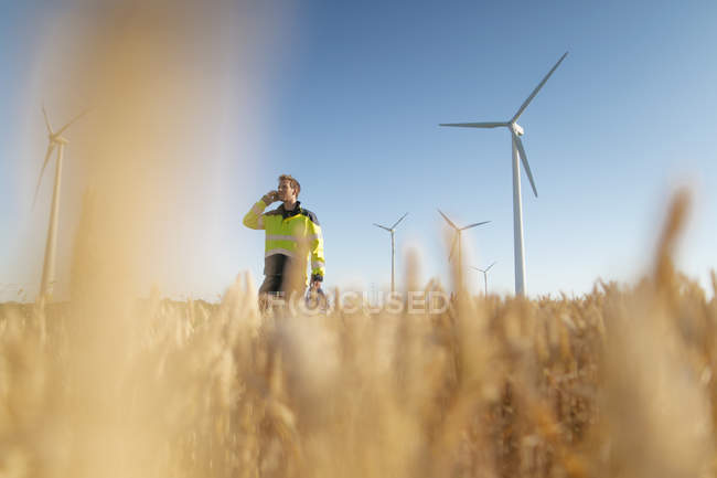 Ingeniero de pie en un campo en un parque eólico y hablando por teléfono celular - foto de stock
