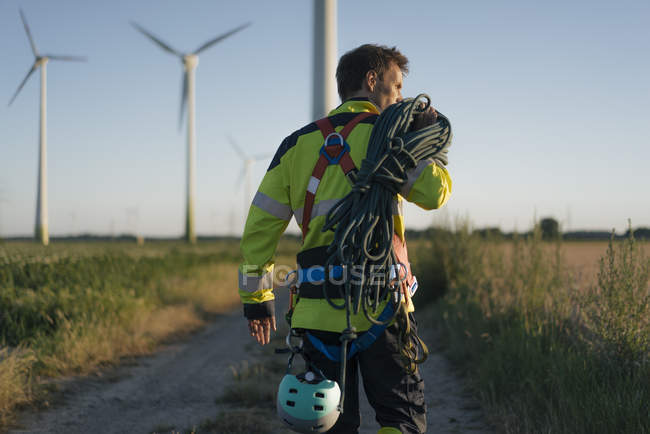 Tecnico che cammina sul campo in un parco eolico con attrezzatura da arrampicata — Foto stock