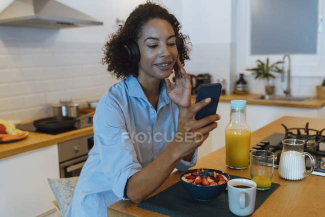 Woman with headphones, using smartphone in her kitchen — Stock Photo