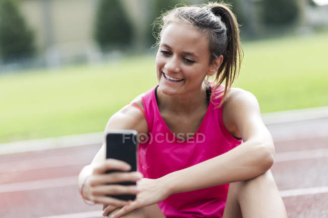 Ragazza adolescente seduta in pista, utilizzando lo smartphone — Foto stock