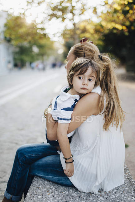 Mutter sitzt auf Bank und umarmt ihren Sohn — Stockfoto