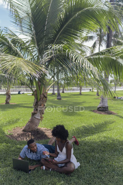 США, Флорида, Майами-Бич, молодая пара с планшетом и ноутбуком на лавке в парке — стоковое фото