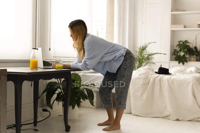 Jovem mulher de pé no quarto em casa usando laptop — Fotografia de Stock