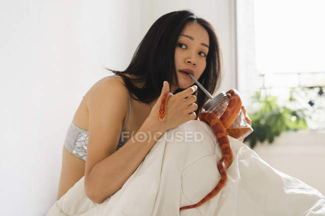 Giovane donna a letto con un serpente e un drink — Foto stock