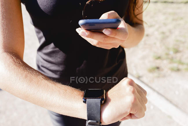 Primer plano de la joven deportista utilizando el teléfono celular y smartwatch - foto de stock