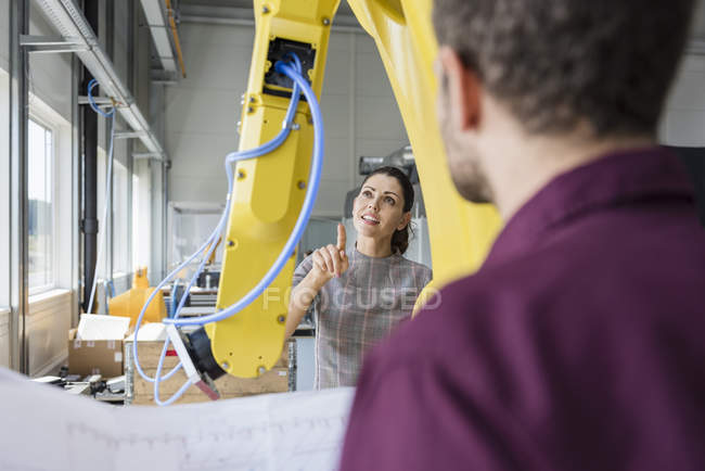 Businessman and woman having a meeting in front of industrial robots in a high tech company — Stock Photo