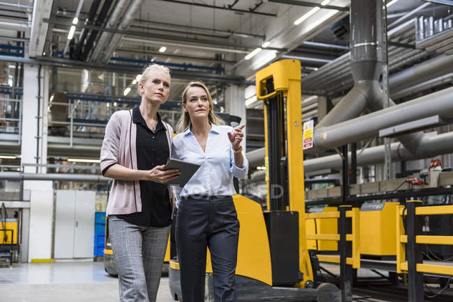 Zwei Frauen mit Tablet gehen und sprechen in der Fabrikhalle — Stockfoto