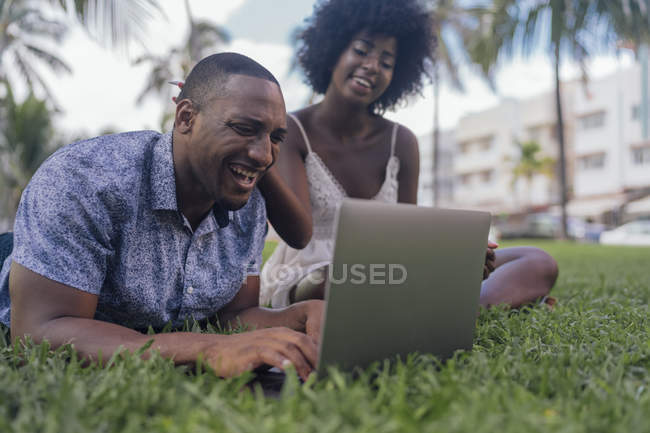 USA, Florida, Miami Beach, ridendo giovane coppia guardando computer portatile sul prato in un parco — Foto stock
