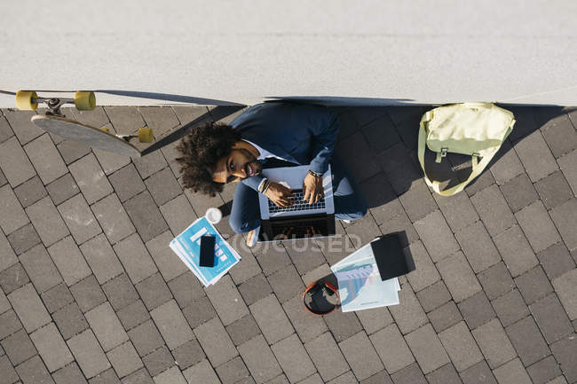 Young businessman sitting outdoors at a wall and working on laptop — Stock Photo