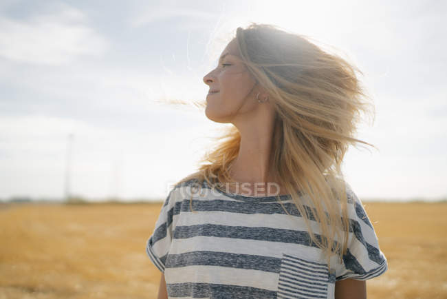 Retrato de una joven sonriente en el paisaje rural agitando el pelo rubio - foto de stock