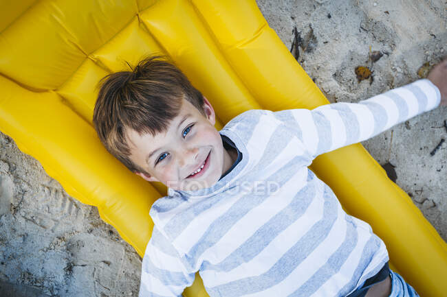 Retrato de un niño sonriente acostado en un airbed amarillo en la playa en otoño - foto de stock