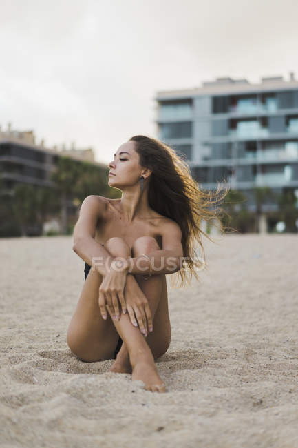 Belle jeune femme assise sur la plage au coucher du soleil — Photo de stock