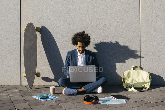 Giovane uomo d'affari seduto all'aperto a un muro e lavorare sul computer portatile — Foto stock
