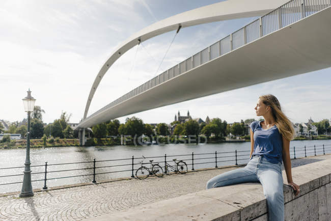 Paesi Bassi, Maastricht, giovane donna seduta su un muro sul lungofiume — Foto stock